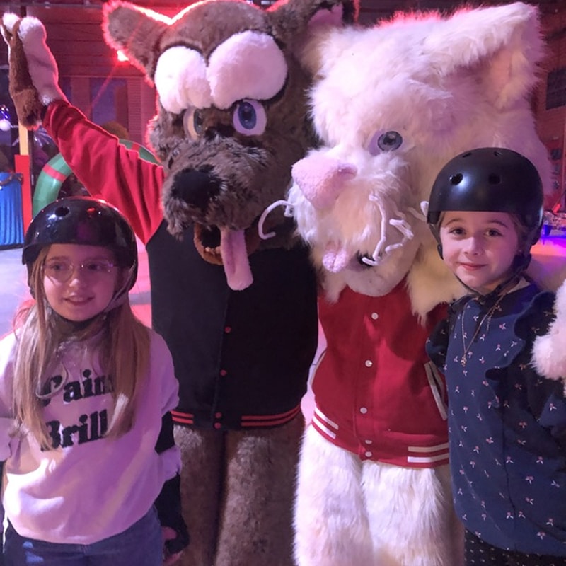 Mascottes et enfants en casque, rencontre amusante Deux fillettes portant des casques de protection posent avec deux mascottes à fourrure, l'une brune et l'autre blanche, lors d'un événement.