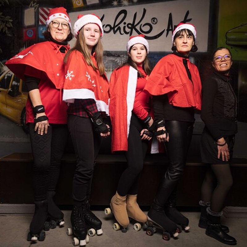 Patins à roulettes et Noël : groupe de femmes stylées Cinq femmes en tenue rouge et bonnets de Noël, certaines portant des patins à roulettes, posent devant un mur avec l'inscription "Kohiko Art".