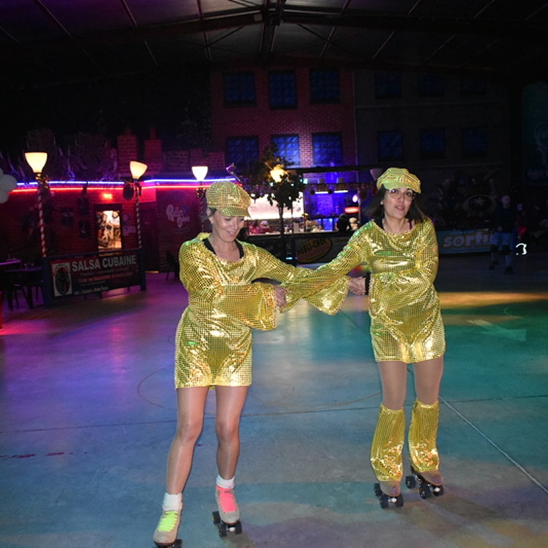 Duo disco en rollers, tenues dorées, ambiance salsa Deux femmes en patins à roulettes, vêtues de tenues dorées à paillettes et casquettes, se tenant la main dans une patinoire colorée avec l'inscription "SALSA CUBAINE".