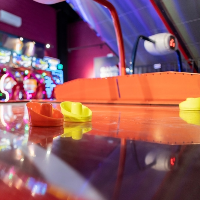 Palets d'air hockey rouge et jaune sur la table brillante d'un jeu d'arcade. Scoreur numérique et lumières néon vives en arrière-plan.