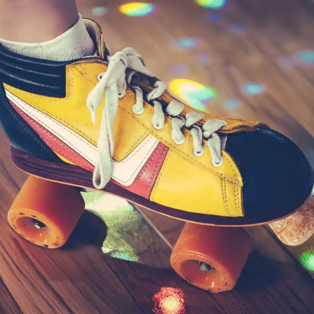 Patin à roulettes quad rétro jaune et rouge sur une piste de bois. Roues oranges et lacets blancs sous des reflets de lumières disco.
